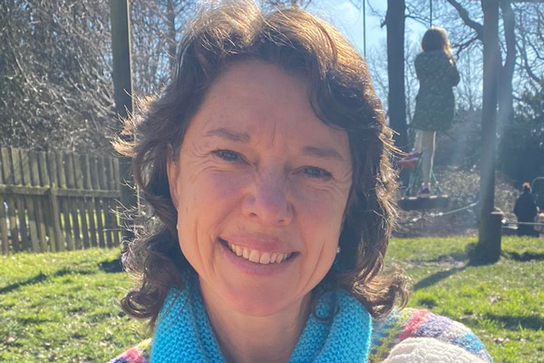 smiling woman outdoors in sunny park enjoying nature with colorful scarf and sweater sitting on grass surrounded by children playing four seasons activities